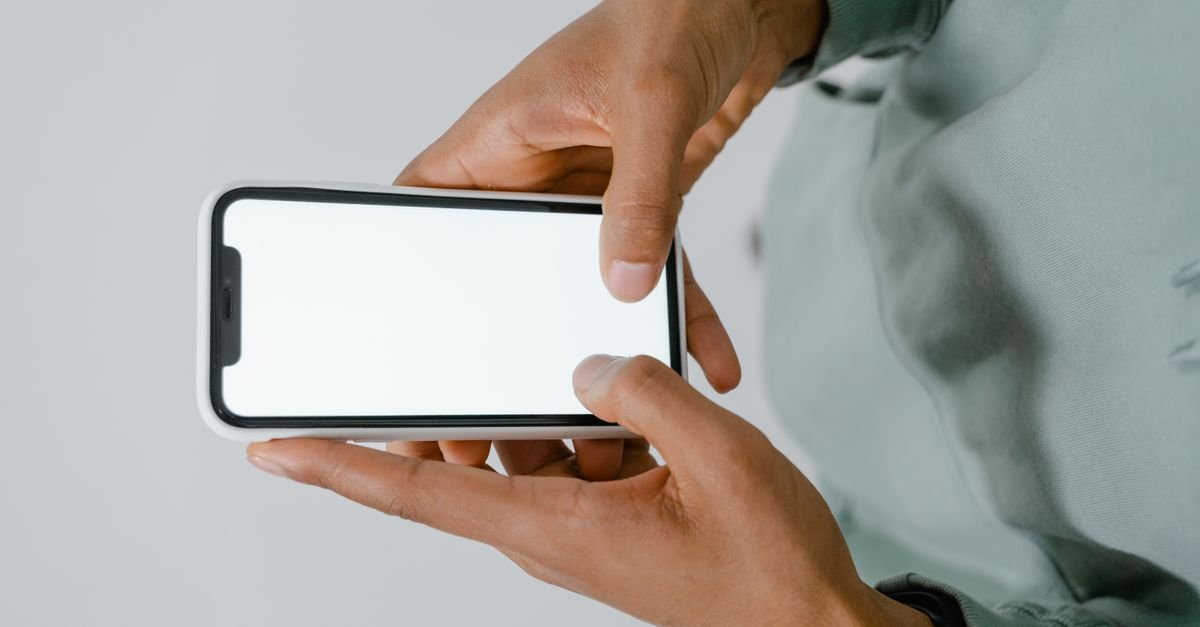 Mãos segurando um celular na horizontal com a tela em branco, sem aplicativo aberto