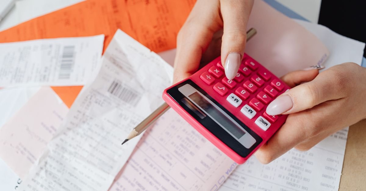 Mãos usando calculadora sobre cupons fiscais e documentos espalhados na mesa