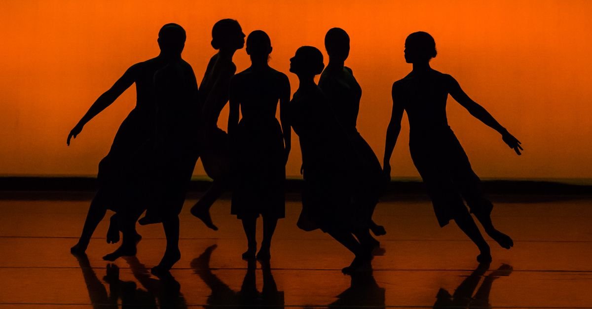 Silhuetas de bailarinos em cena de dança contemporânea sobre fundo alaranjado