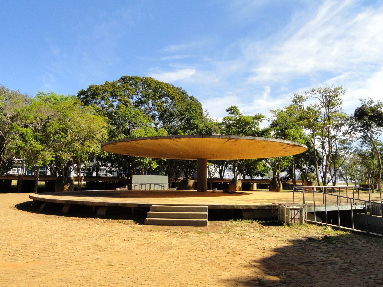 Palco circular ao ar livre sob uma grande cobertura de concreto, entre árvores, em área do Clube do Choro de Brasília