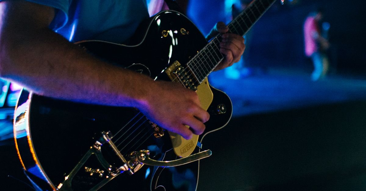 Guitarrista toca guitarra elétrica em close durante show noturno