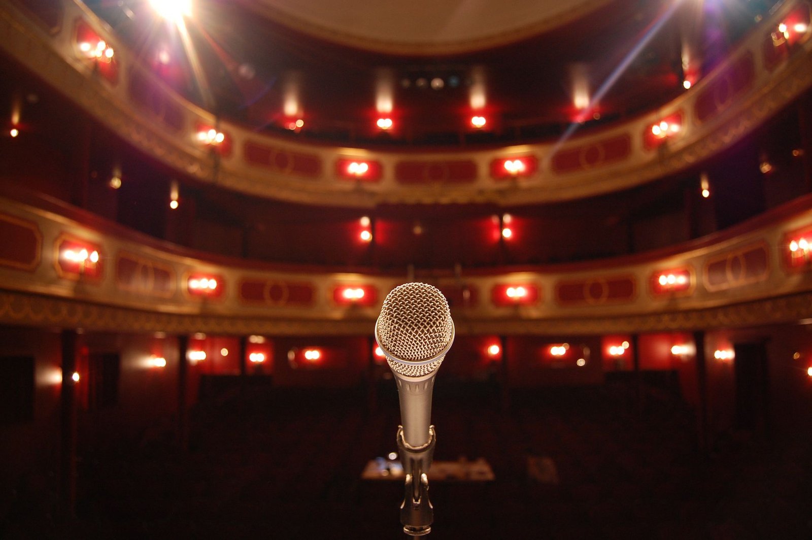 Microfone no palco de um teatro com balcões em vermelho e dourado ao fundo