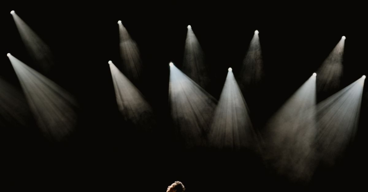 Refletores acesos sobre palco escuro durante apresentação teatral