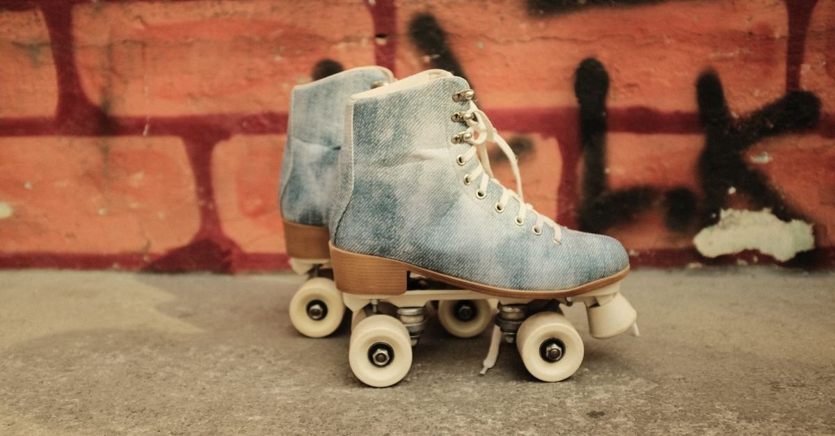 Par de patins de quatro rodas em jeans apoiado no chão de concreto diante de um muro de tijolos