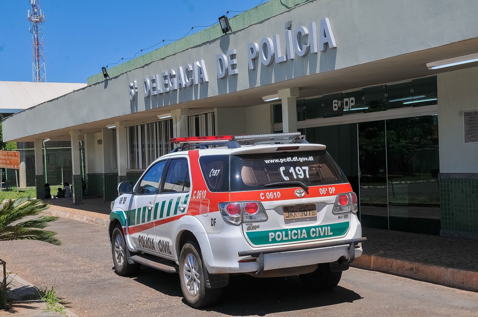 Viatura branca da Polícia Civil do Distrito Federal estacionada em frente à fachada de uma delegacia de polícia