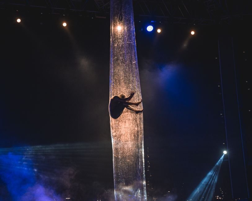 Artista de tecido acrobático suspensa no palco sob iluminação cênica
