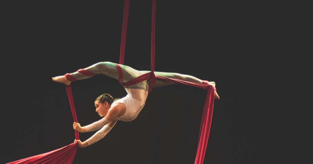 Artista de circo aéreo executa movimento suspenso em tecido vermelho