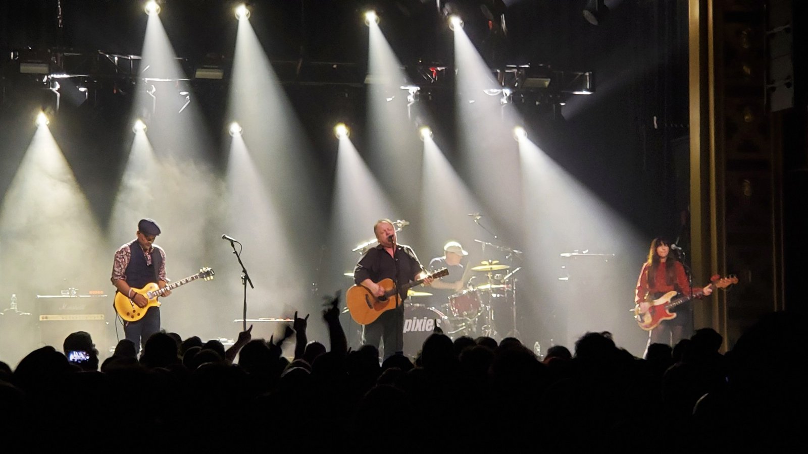 Pixies em show em 2019, com guitarrista, vocalista e baixista sob feixes de luz no palco (foto de arquivo)