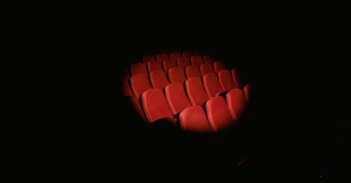 Poltronas vermelhas de teatro iluminadas por refletor em sala escura