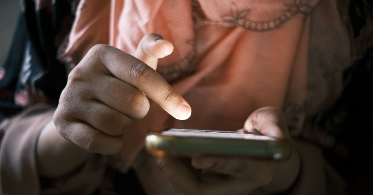 Mãos segurando e tocando a tela de um celular em ambiente interno