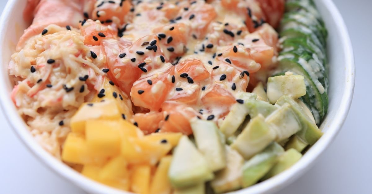 Poke bowl com salmão, manga, pepino, abacate e gergelim servido em tigela branca