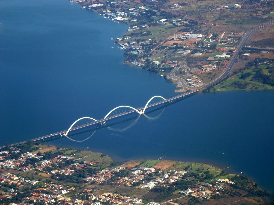 Vista aérea da Ponte JK cruzando o Lago Paranoá, em Brasília, com os três arcos brancos sobre a água