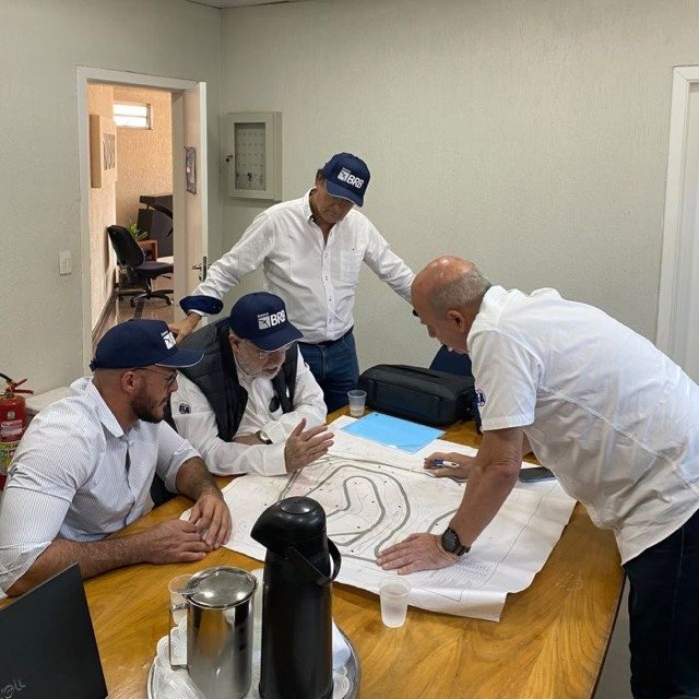 Quatro homens em volta de uma mesa analisam a planta do traçado do autódromo