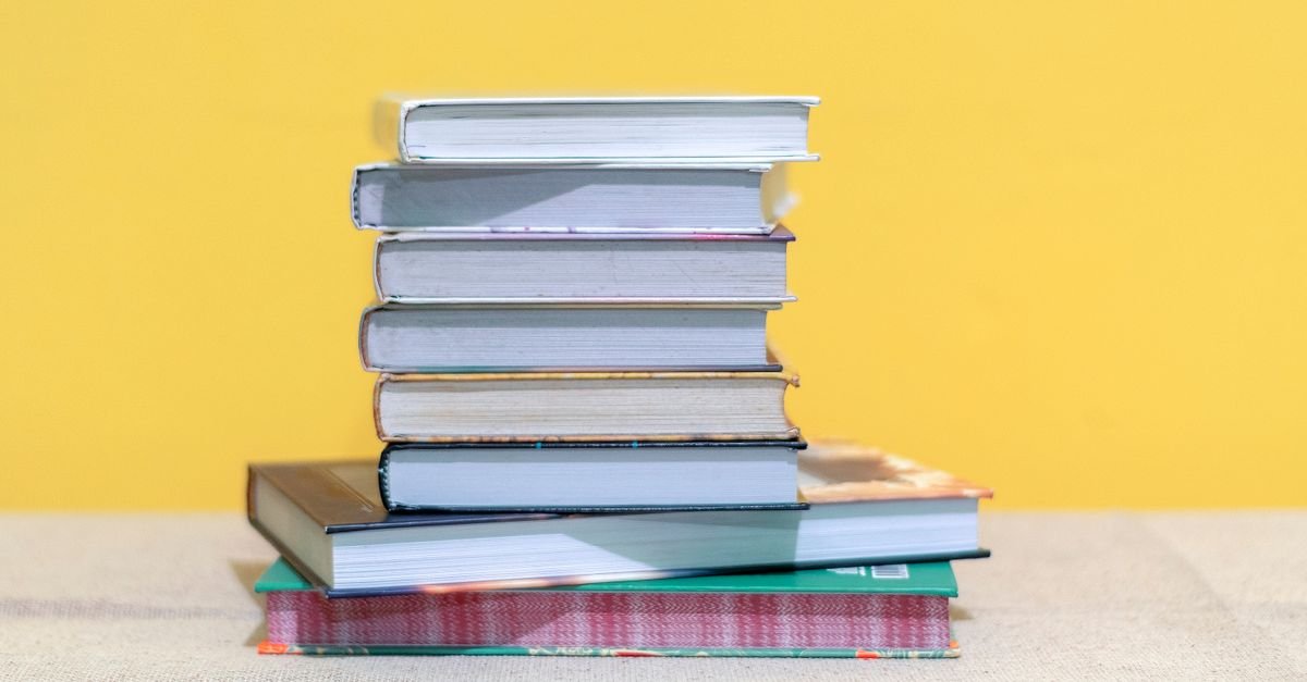 Pilha de livros de capa dura sobre mesa clara com fundo amarelo