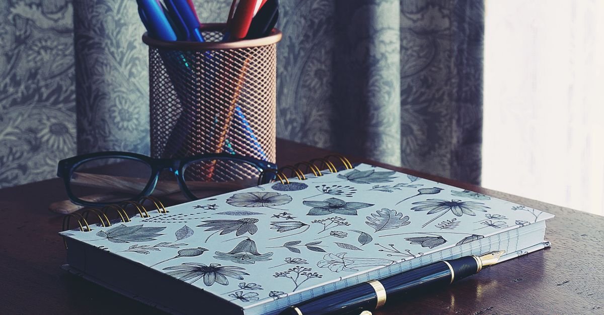 Caderno fechado, óculos e porta-canetas sobre mesa de madeira