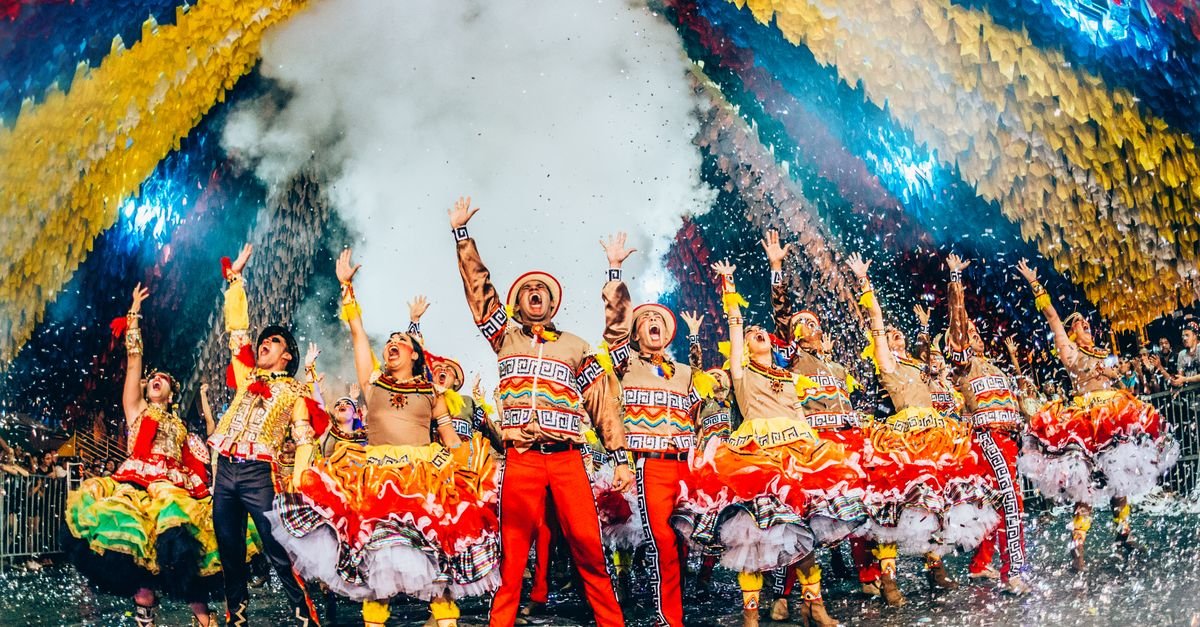 Dançarinos de quadrilha junina com trajes coloridos se apresentam sob bandeirinhas