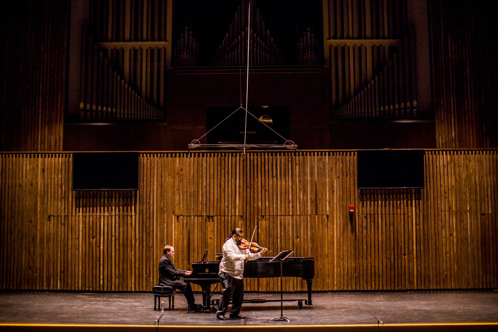 Violinista e pianista em palco de teatro com órgão ao fundo