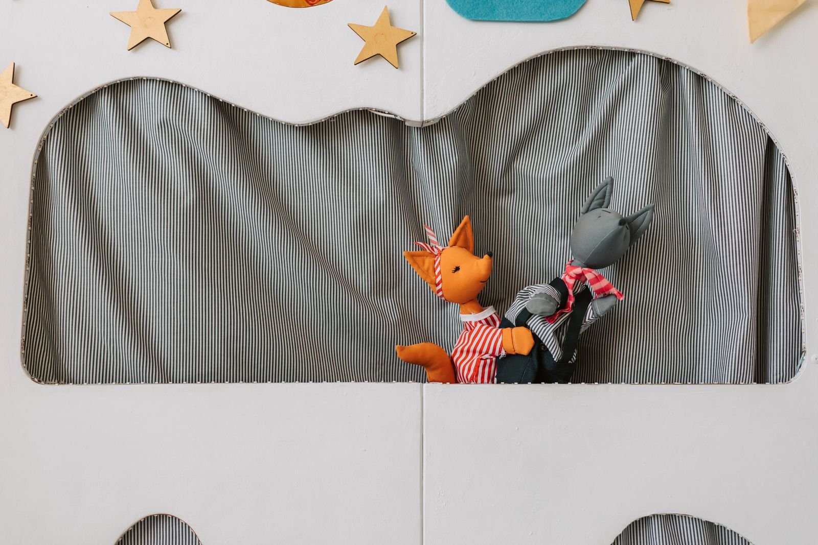 Bonecos de raposa laranja e lobo cinza em teatro de fantoches com cortina listrada