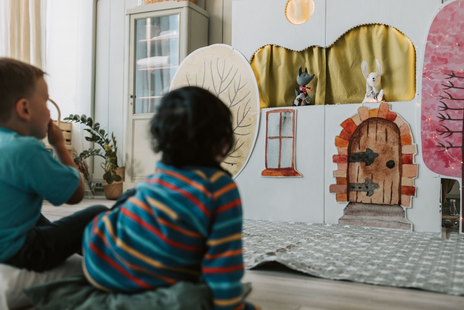 Duas crianças sentadas no chão assistem a um teatro de fantoches