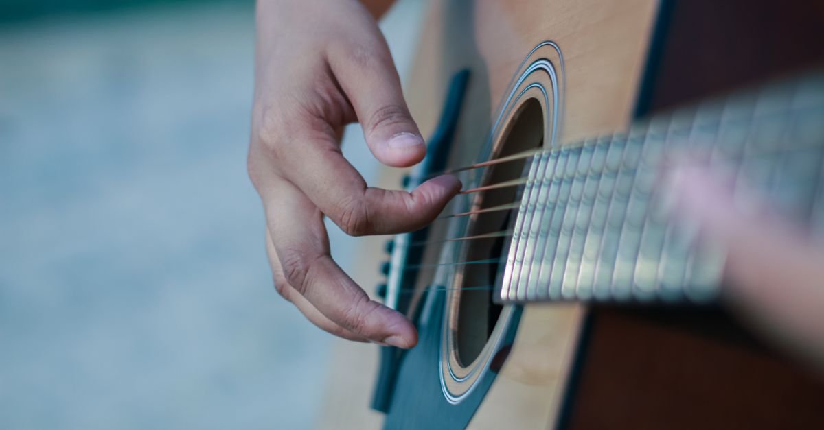 Close das maos de uma pessoa dedilhando as cordas de um violao acustico