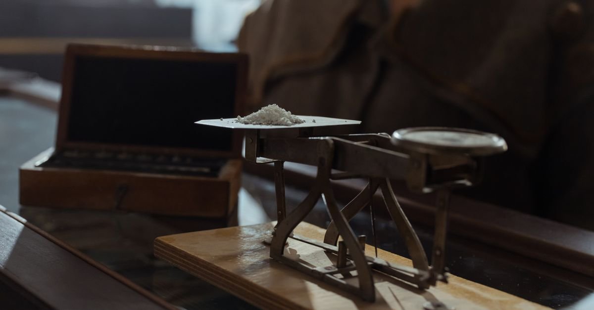 Balança de pratos com pequena porção de pó branco sobre mesa de madeira