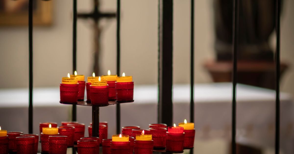 Velas votivas vermelhas diante de uma cruz em igreja, imagem ilustrativa