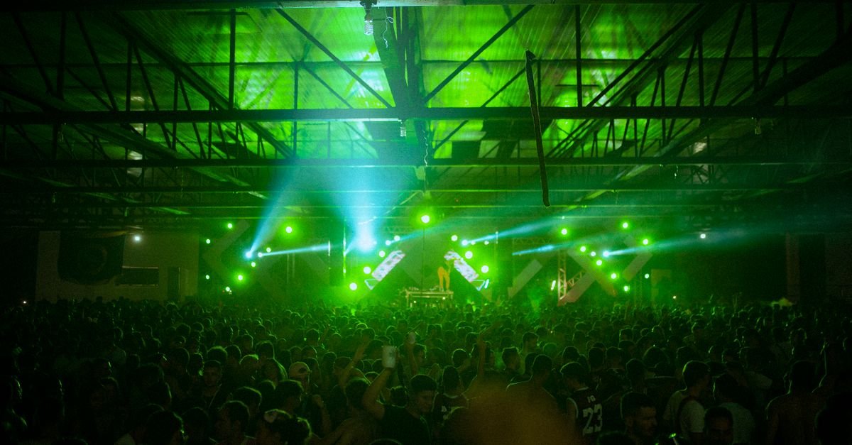 Público em festa de música eletrônica sob luzes verdes em galpão