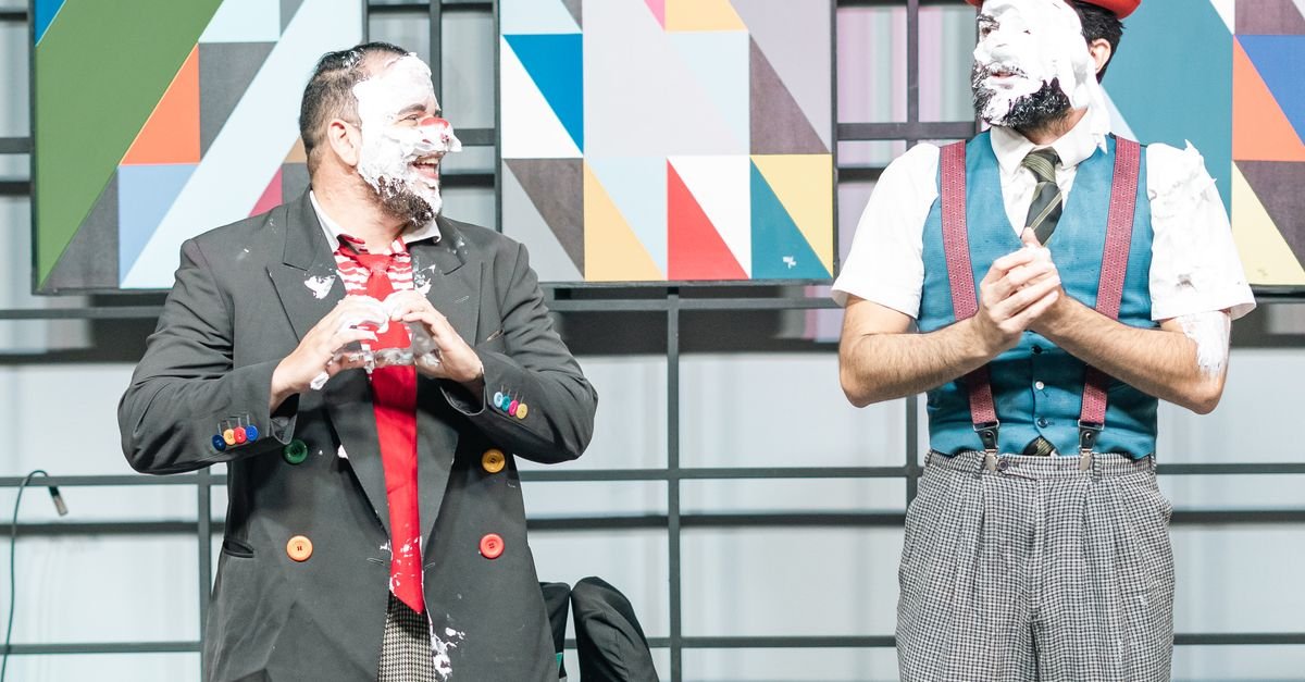 Dois palhaços em cena com o rosto coberto de espuma branca durante apresentação teatral