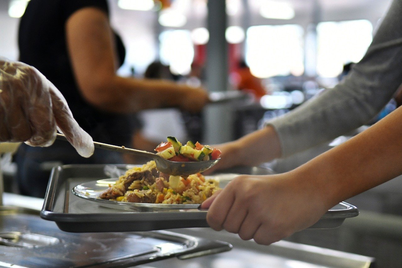 Funcionário serve prato de arroz com carne e salada em restaurante comunitário do DF