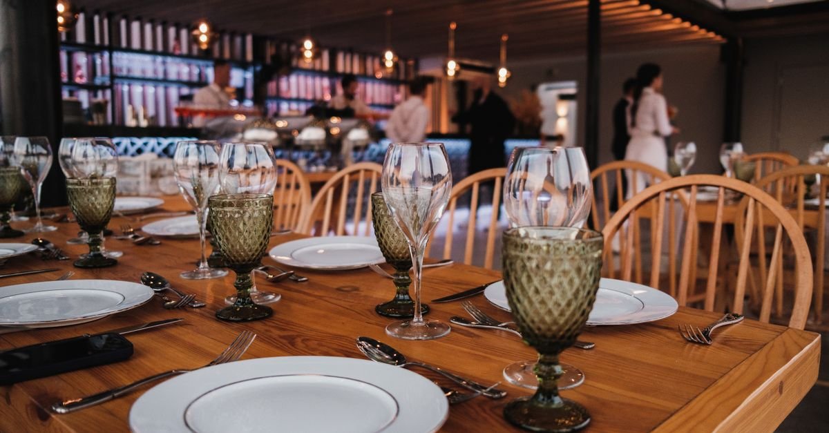 Mesa de madeira posta com taças e pratos em um restaurante, imagem ilustrativa