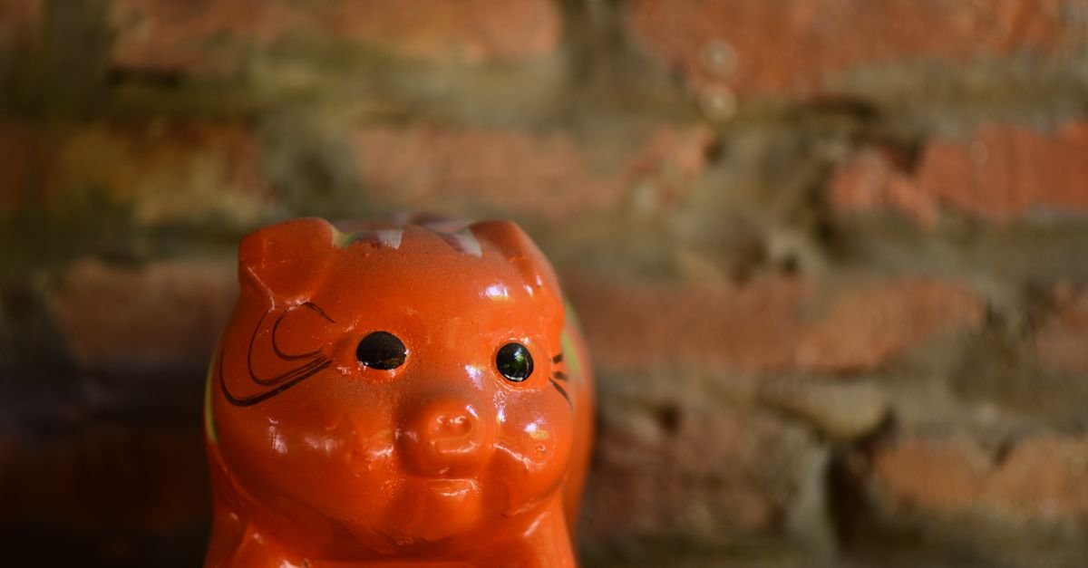 Cofrinho de cerâmica laranja em prateleira diante de parede de tijolos