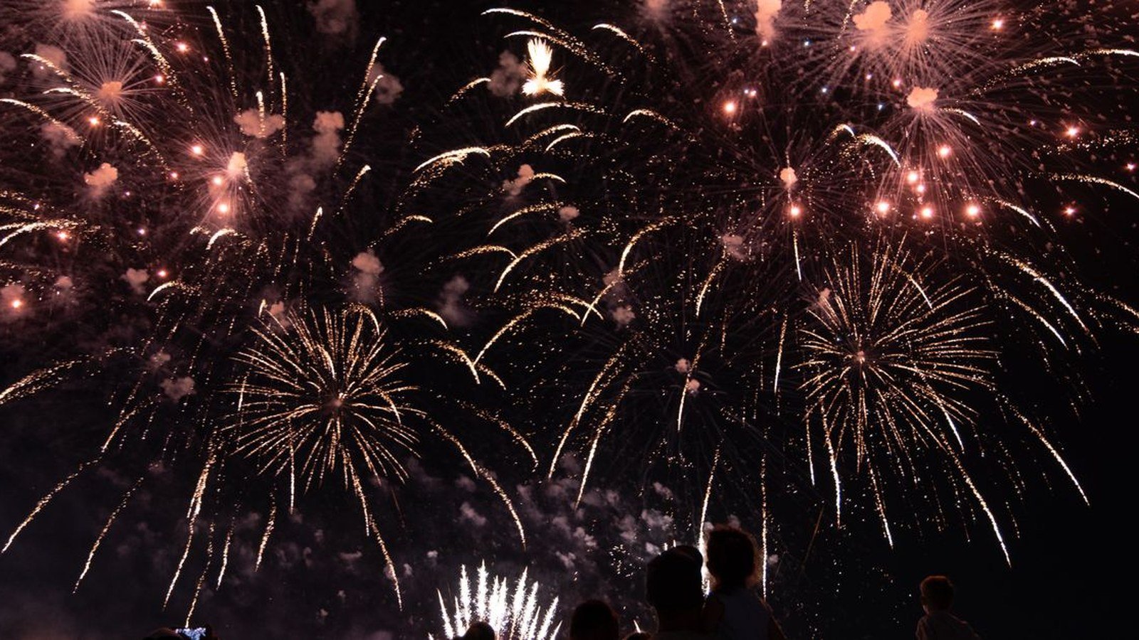 Silhuetas de uma multidão assistindo a uma queima de fogos no céu noturno