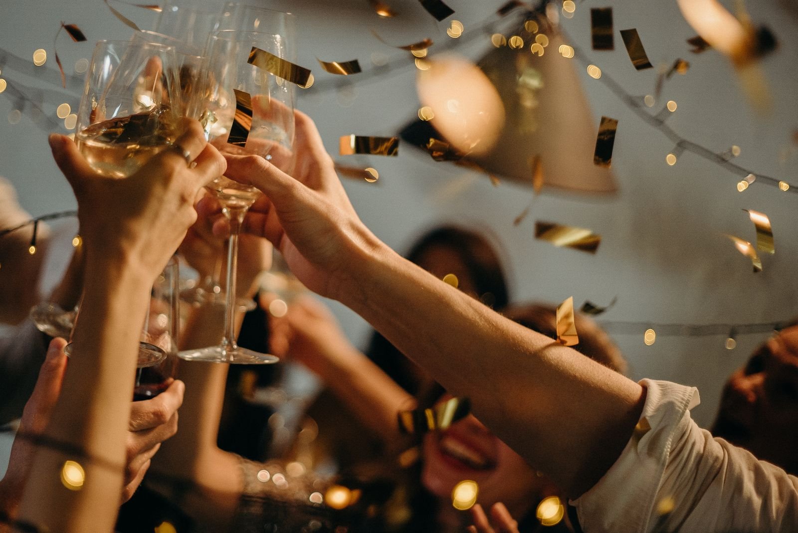 Mãos brindando com taças sob confete dourado em festa de fim de ano