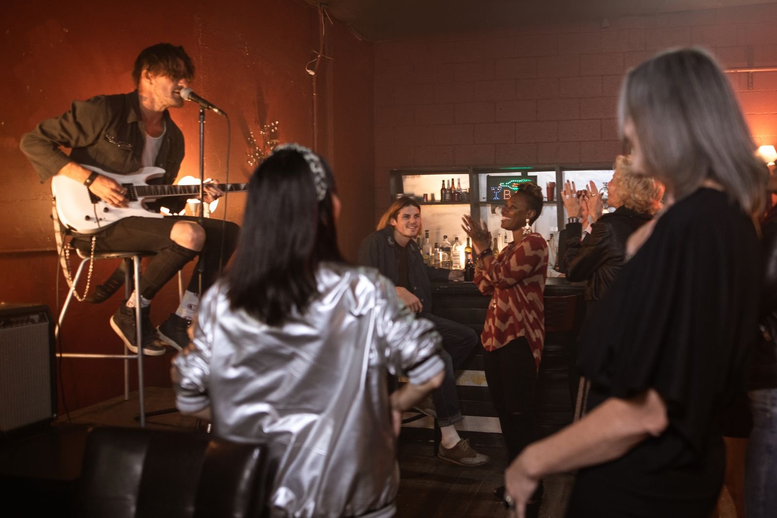 Músico toca guitarra e canta em bar com plateia ao fundo