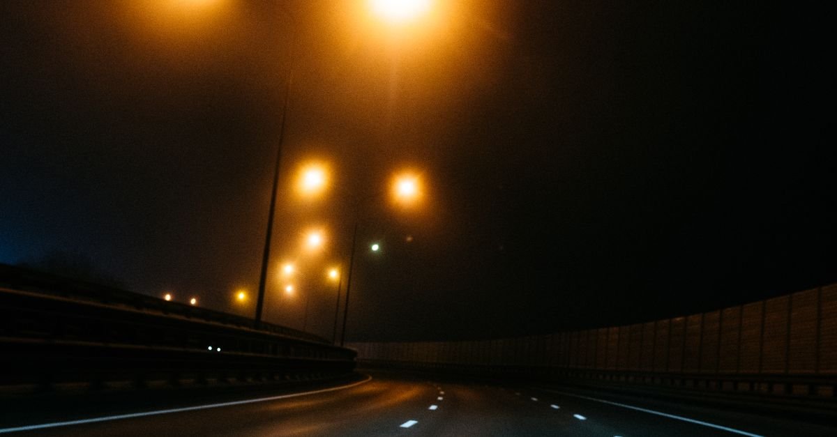 Rodovia de pista dupla à noite, iluminada por postes, sem veículos na faixa