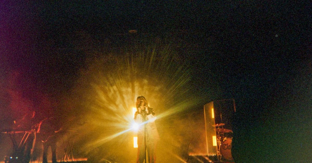 Cantor no centro do palco iluminado por holofote durante show