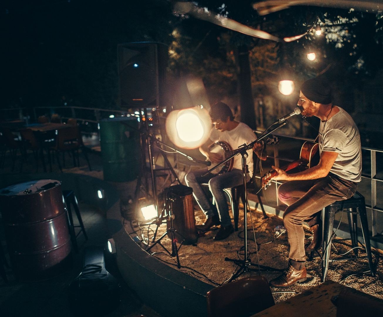 Dois músicos tocando violão e banjo em palco ao ar livre à noite; foto de arquivo ilustrativa