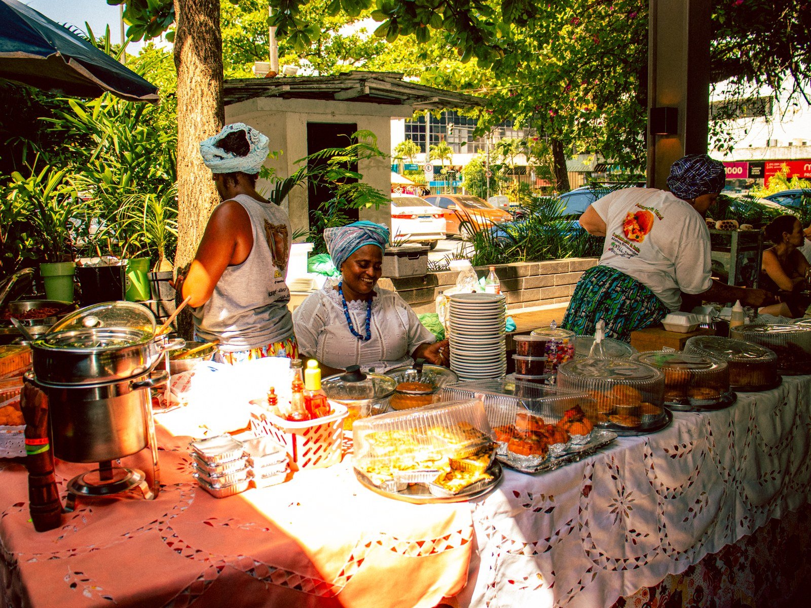 Barraca de baianas com mesa de comidas típicas sob árvores