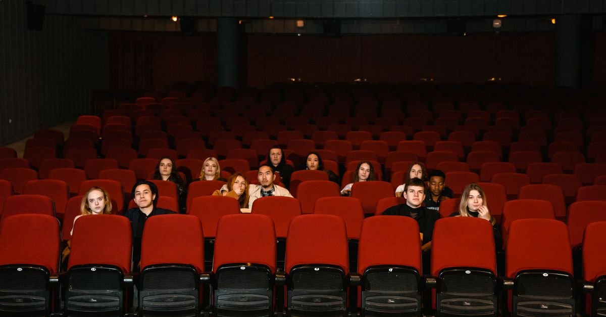 Espectadores sentados em poltronas vermelhas de uma sala de cinema