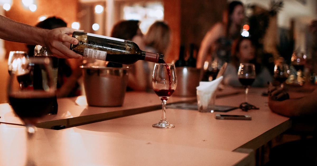 Vinho tinto sendo servido em taça sobre balcão de bar à noite