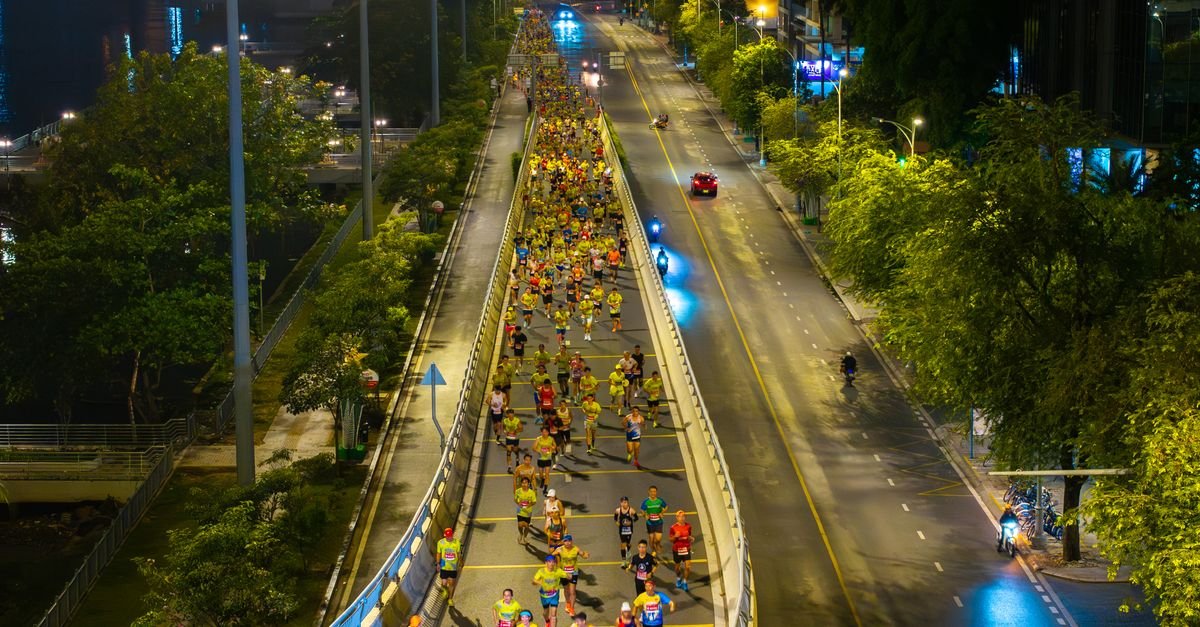Corredores em prova noturna em avenida iluminada, vista de cima