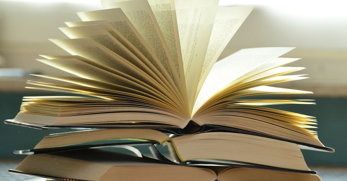 Pilha de livros abertos com as páginas em leque, iluminados por luz natural