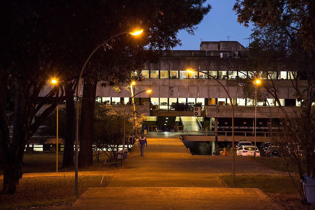 Predio do campus Darcy Ribeiro da UnB iluminado ao anoitecer, com caminho de pedestres em primeiro plano