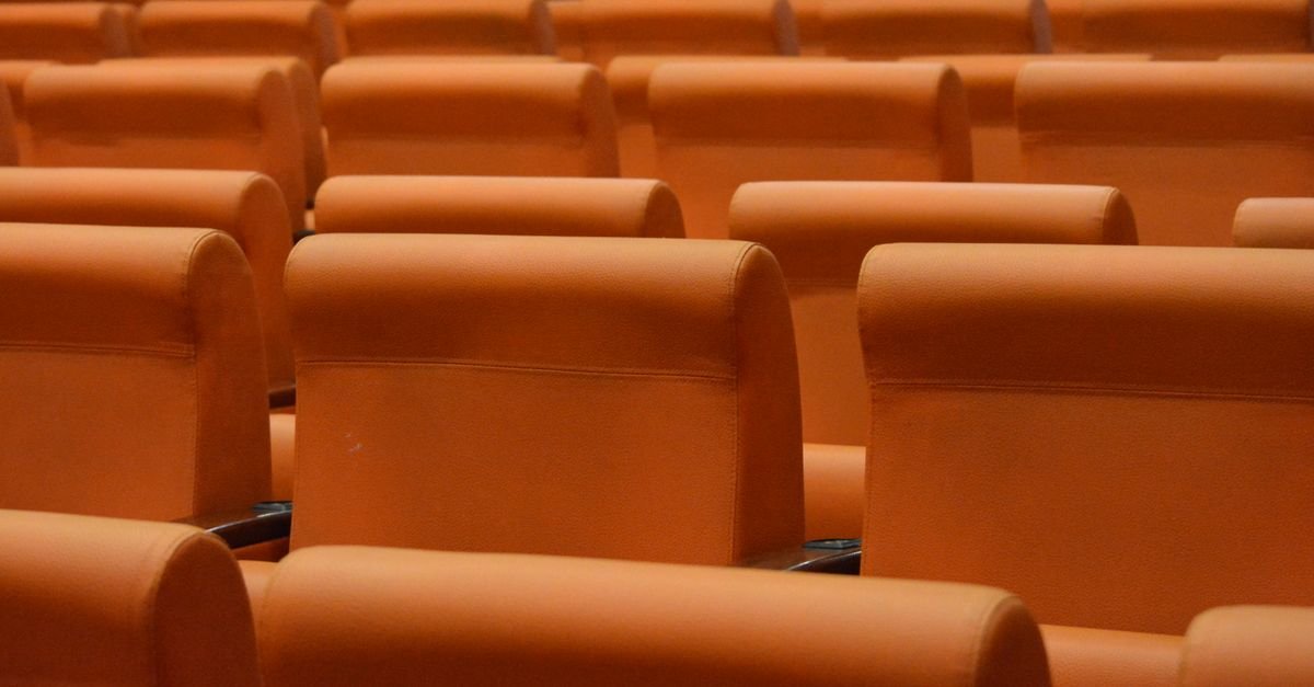 Fileiras de poltronas laranja em auditório vazio