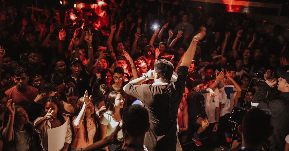 Rapper de costas no palco diante de público com as mãos erguidas durante show