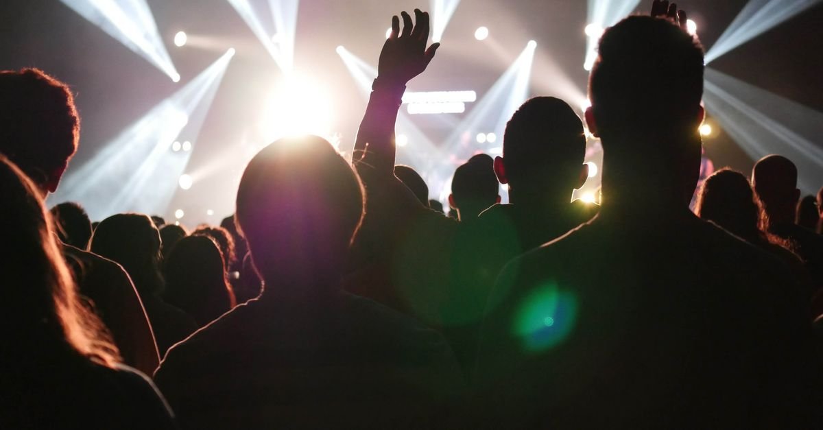 Público em silhueta diante de palco com luzes coloridas durante show