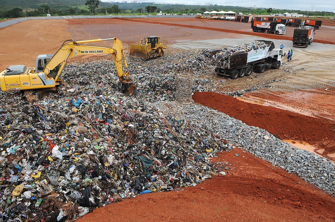 Escavadeira e trator de esteira trabalham sobre lixo em célula do Aterro Sanitário de Brasília, com caminhões ao fundo (foto de arquivo)