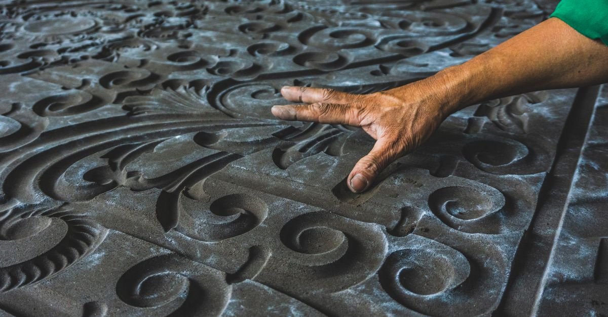 Mão tocando um relevo ornamental esculpido em pedra escura, imagem ilustrativa de arte tátil