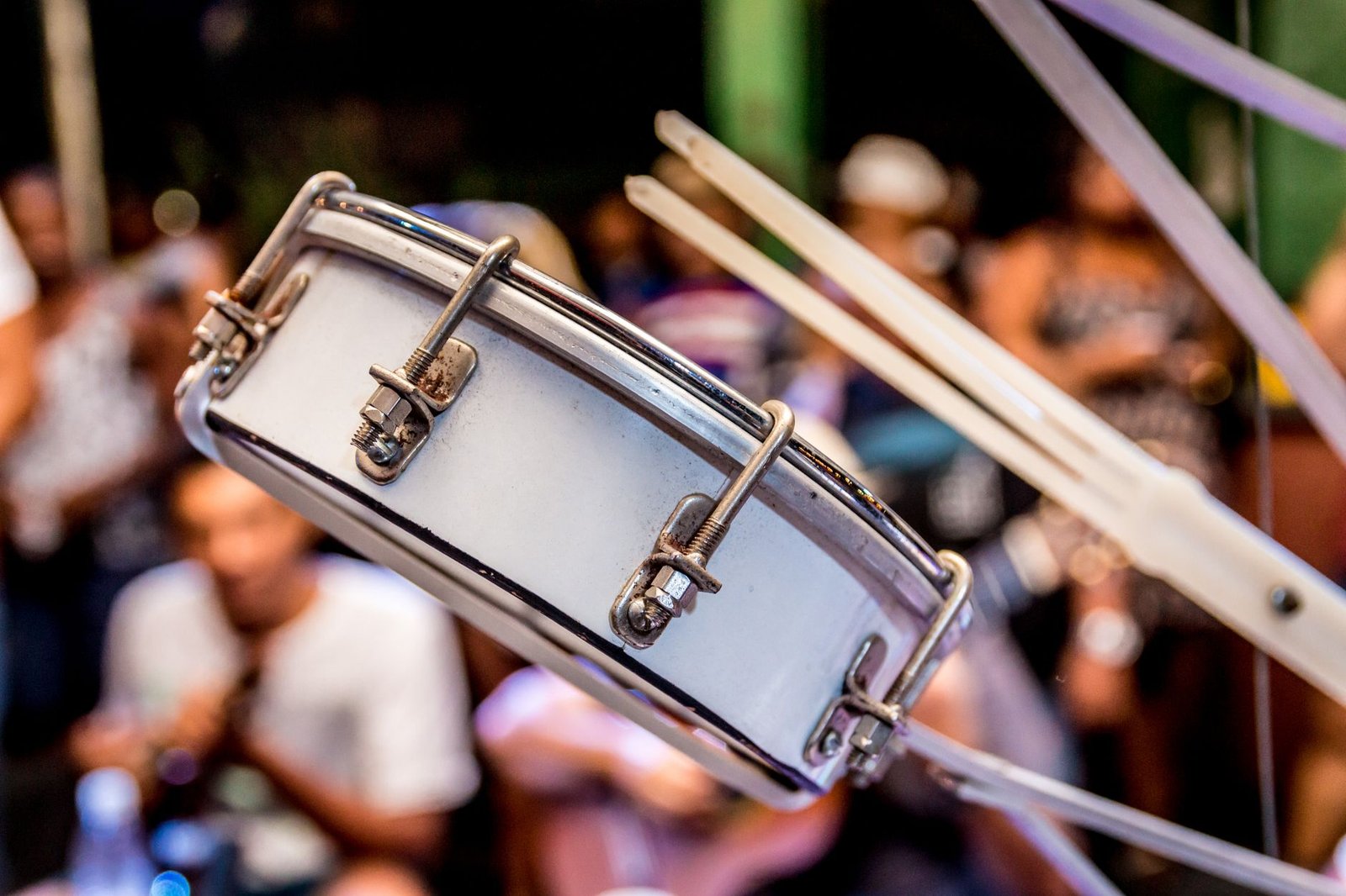 Pandeiro de samba em primeiro plano, com público desfocado ao fundo, em roda de samba