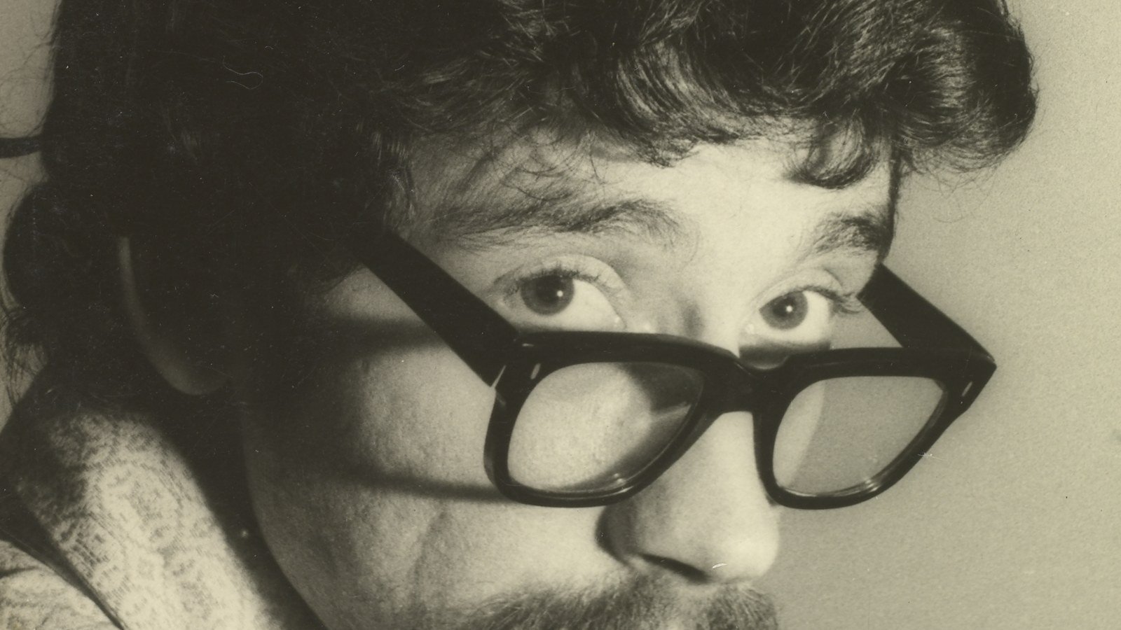 Retrato em preto e branco de Raul Seixas, em 1972, olhando por cima de óculos de aro grosso